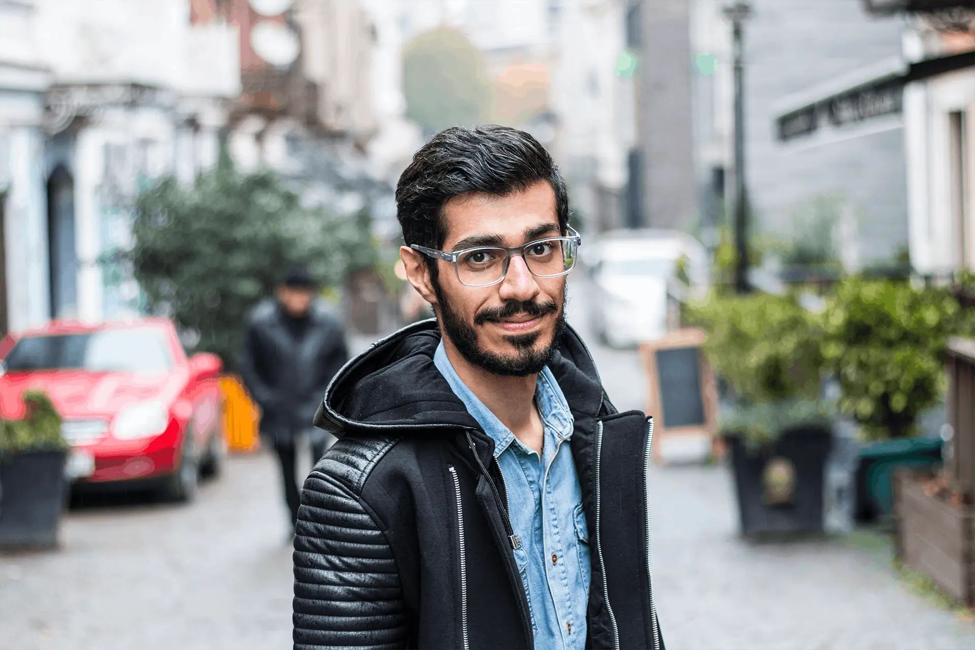 A young man with glasses smiles casually on a street in Tbilisi, Georgia.